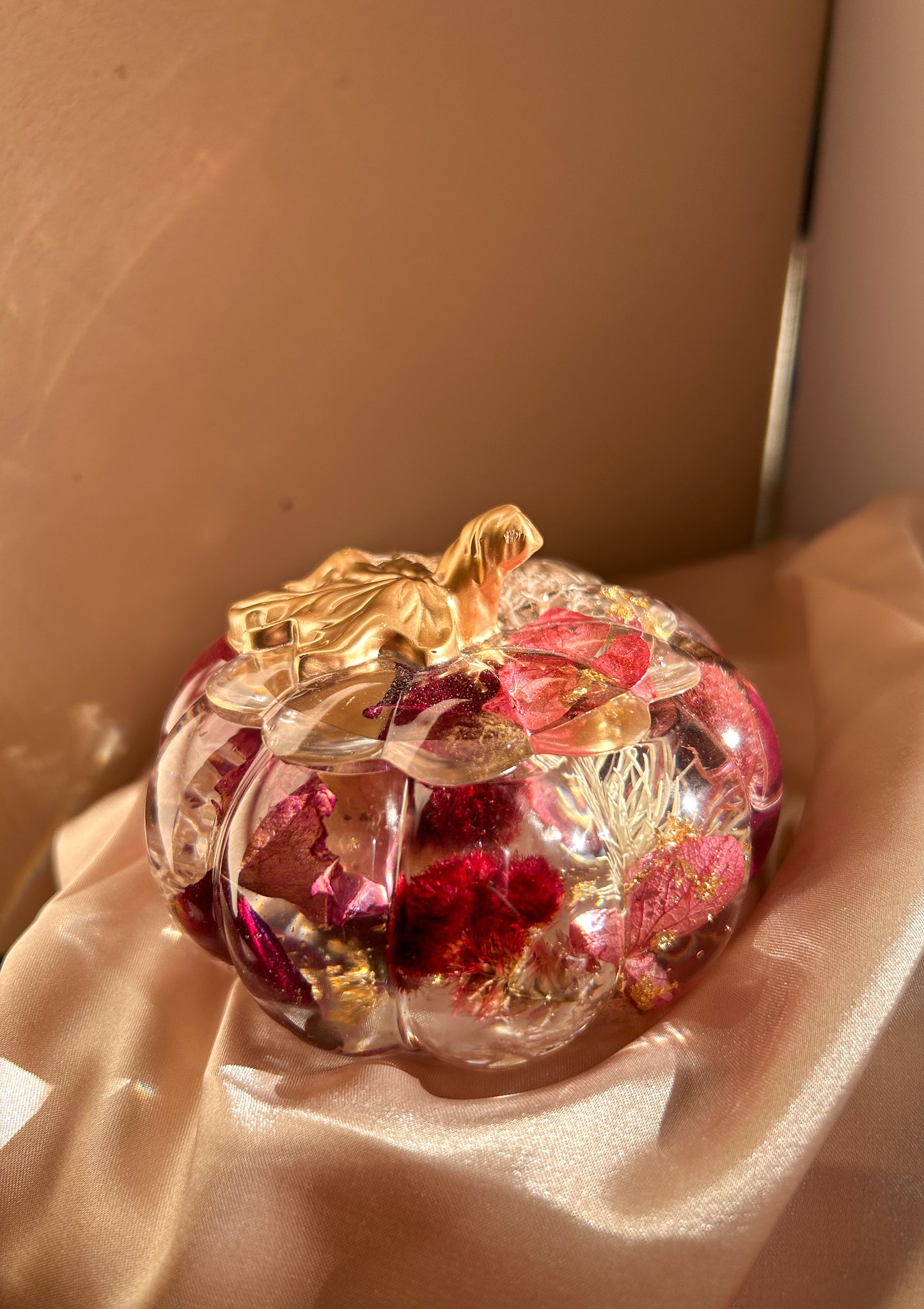 A handmade floral pumpkin-shaped resin jewelry jar with real dried flowers embedded inside. The jar has a smooth, glossy finish and is designed for storing rings, earrings, necklaces, and other small jewelry. Its elegant nature-inspired design makes it a unique decorative piece, perfect for boho or cottagecore home decor.