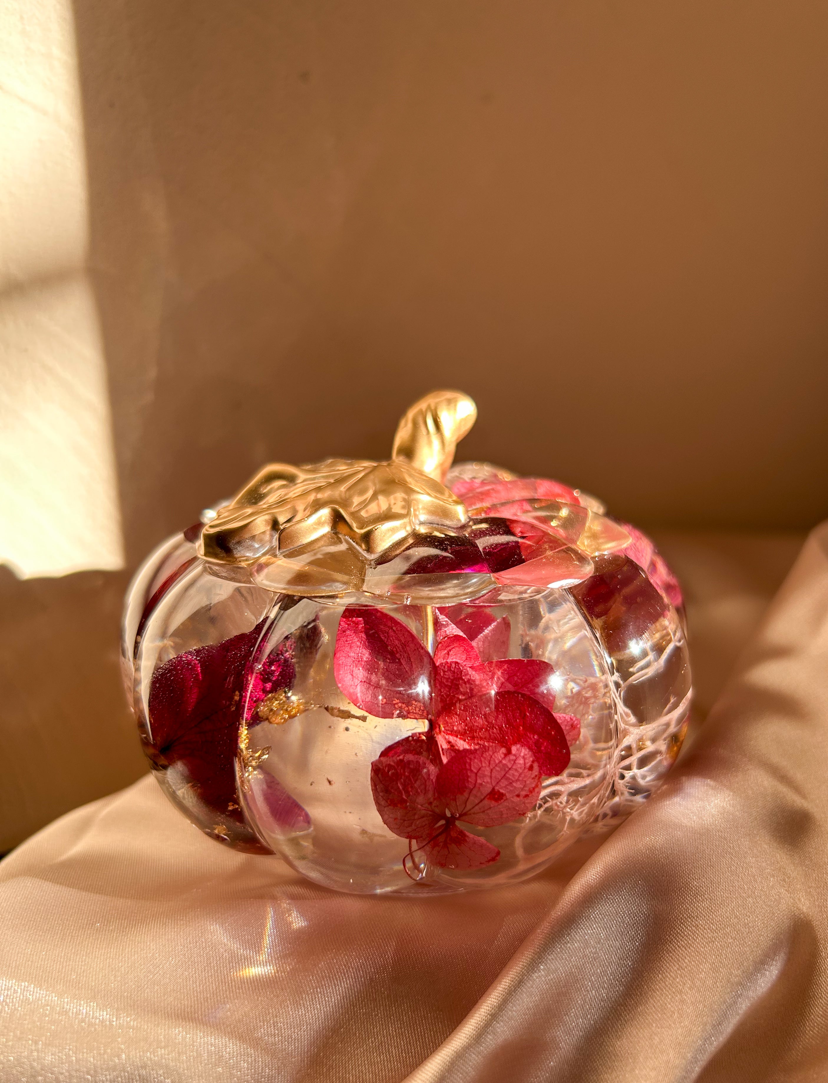 A handmade floral pumpkin-shaped resin jewelry jar with real dried flowers embedded inside. The jar has a smooth, glossy finish and is designed for storing rings, earrings, necklaces, and other small jewelry. Its elegant nature-inspired design makes it a unique decorative piece, perfect for boho or cottagecore home decor.