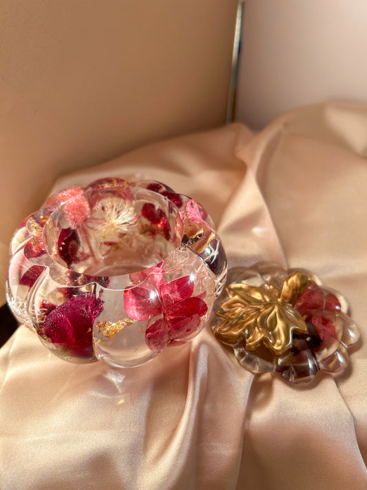 A handmade floral pumpkin-shaped resin jewelry jar with real dried flowers embedded inside. The jar has a smooth, glossy finish and is designed for storing rings, earrings, necklaces, and other small jewelry. Its elegant nature-inspired design makes it a unique decorative piece, perfect for boho or cottagecore home decor.