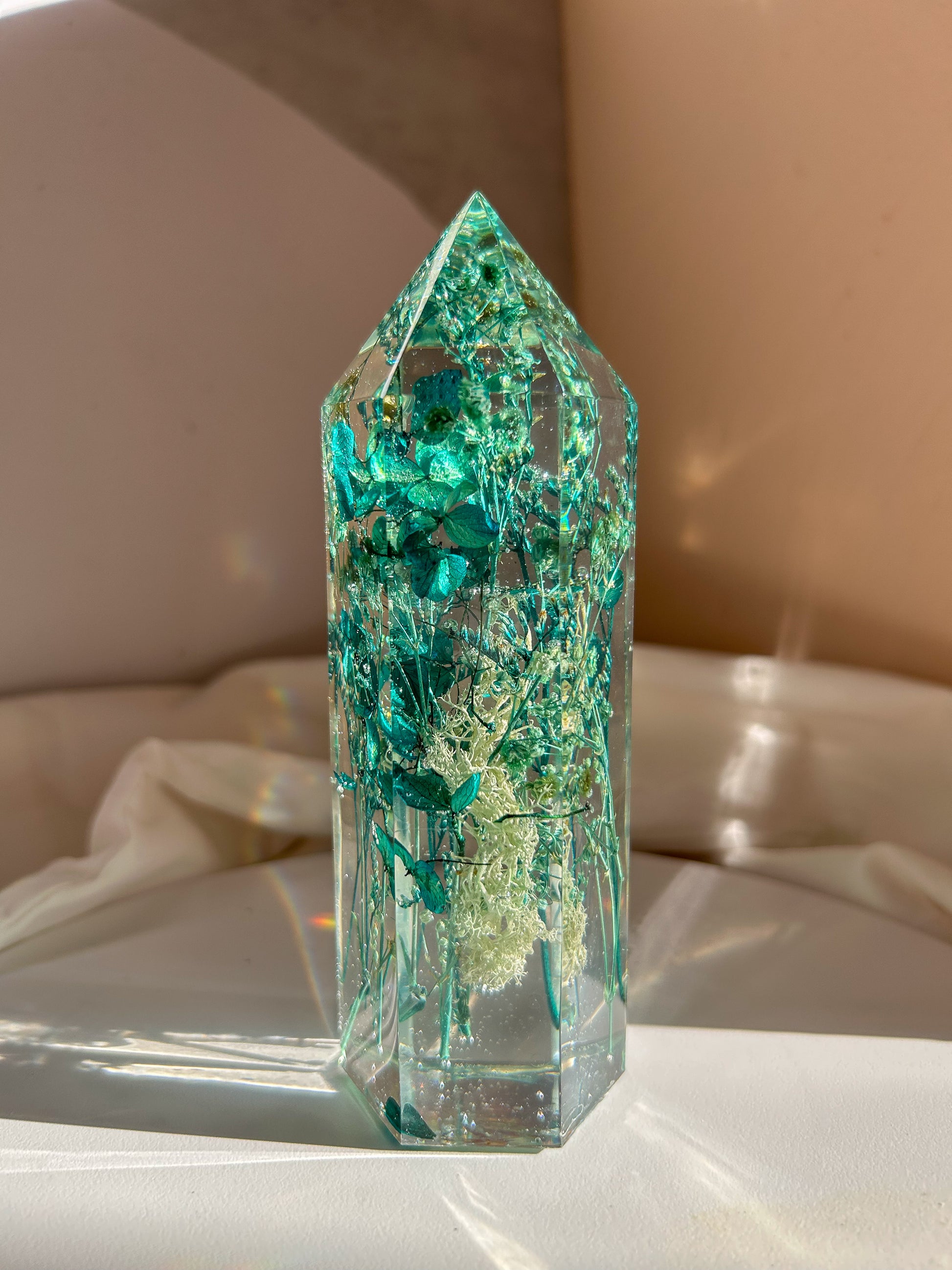 A beautiful handmade epoxy resin crystal made with blue teal, light blue and green natural dried flowers. perfectly cast in crystal clear epoxy resin. Great for home decor, gifts, unique presents, vanity bedroom decor and shelf decor.