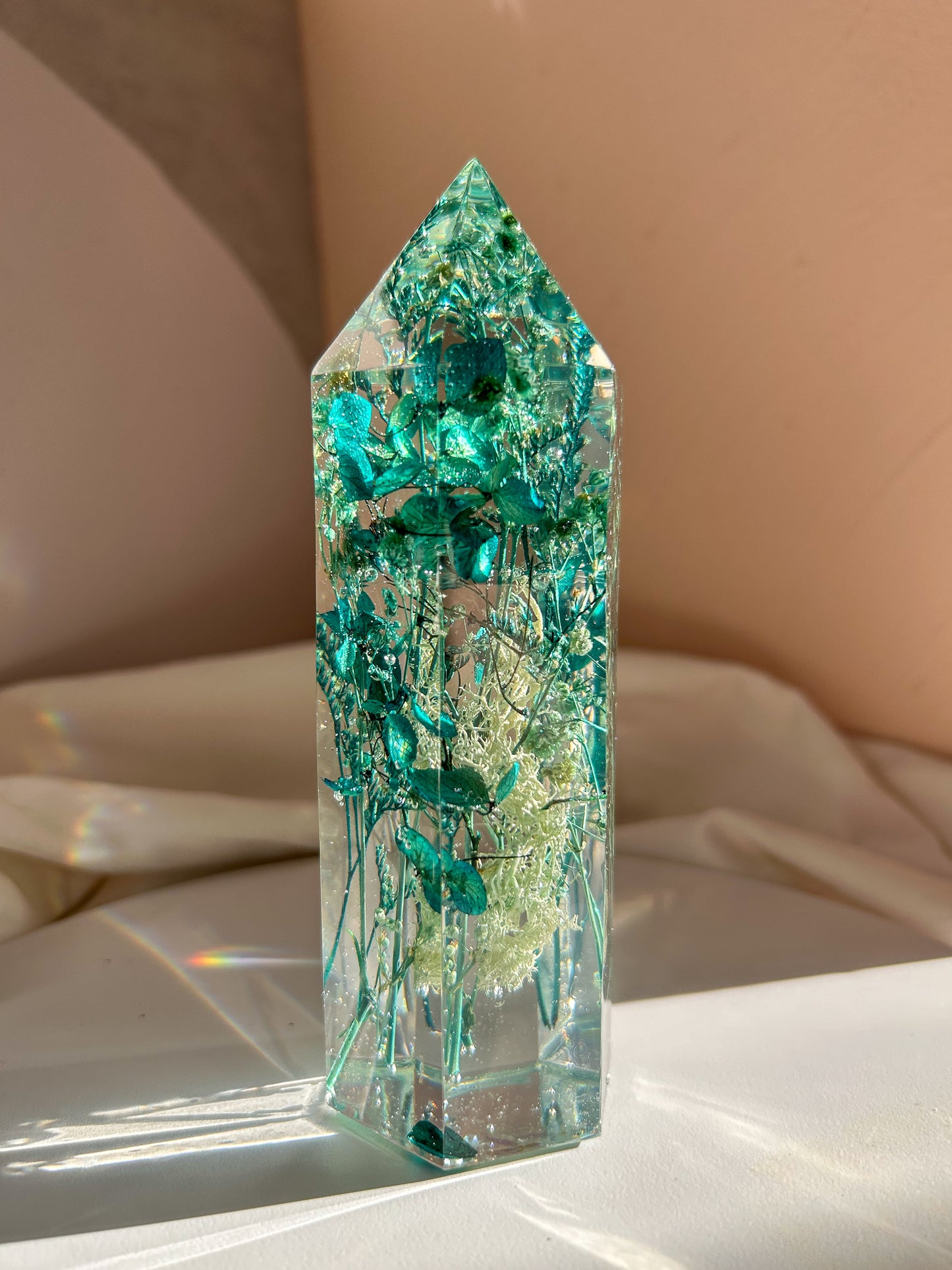 A beautiful handmade epoxy resin crystal made with blue teal, light blue and green natural dried flowers. perfectly cast in crystal clear epoxy resin. Great for home decor, gifts, unique presents, vanity bedroom decor and shelf decor.