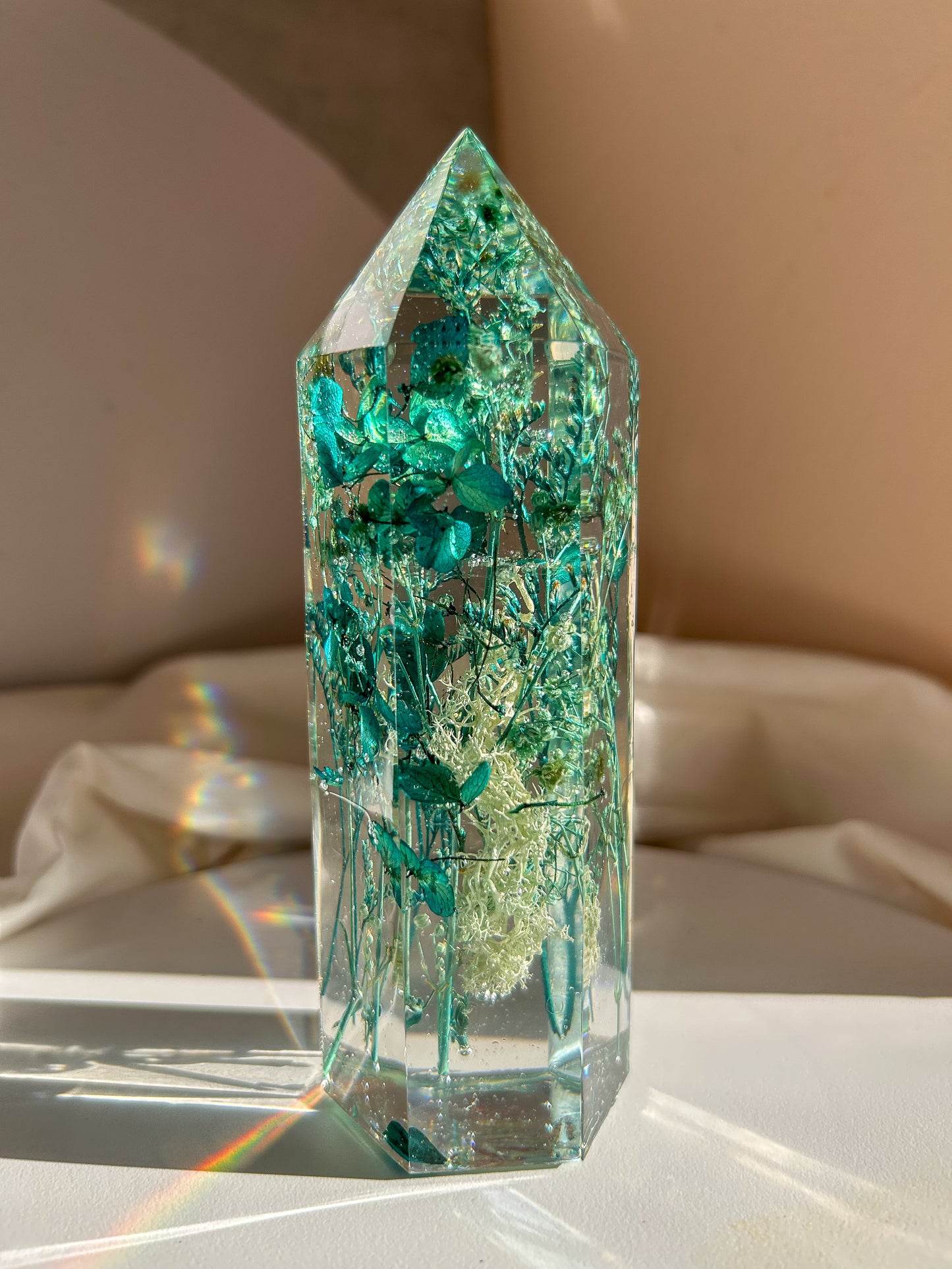 A beautiful handmade epoxy resin crystal made with blue teal, light blue and green natural dried flowers. perfectly cast in crystal clear epoxy resin. Great for home decor, gifts, unique presents, vanity bedroom decor and shelf decor.