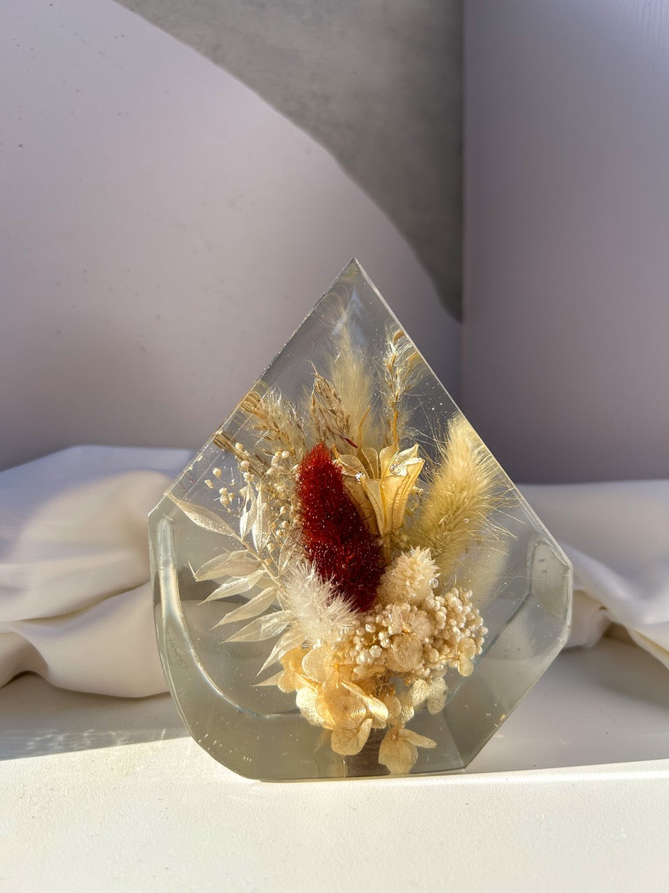 Gem-shaped resin decor featuring a preserved bouquet of dried flowers, including a striking burgundy red flower, all encased in clear resin. Handmade botanical art, perfect for unique home decor or as a thoughtful gift.