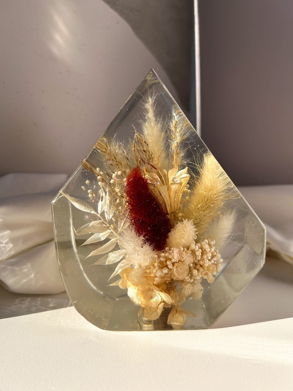 Gem-shaped resin decor featuring a preserved bouquet of dried flowers, including a striking burgundy red flower, all encased in clear resin. Handmade botanical art, perfect for unique home decor or as a thoughtful gift.