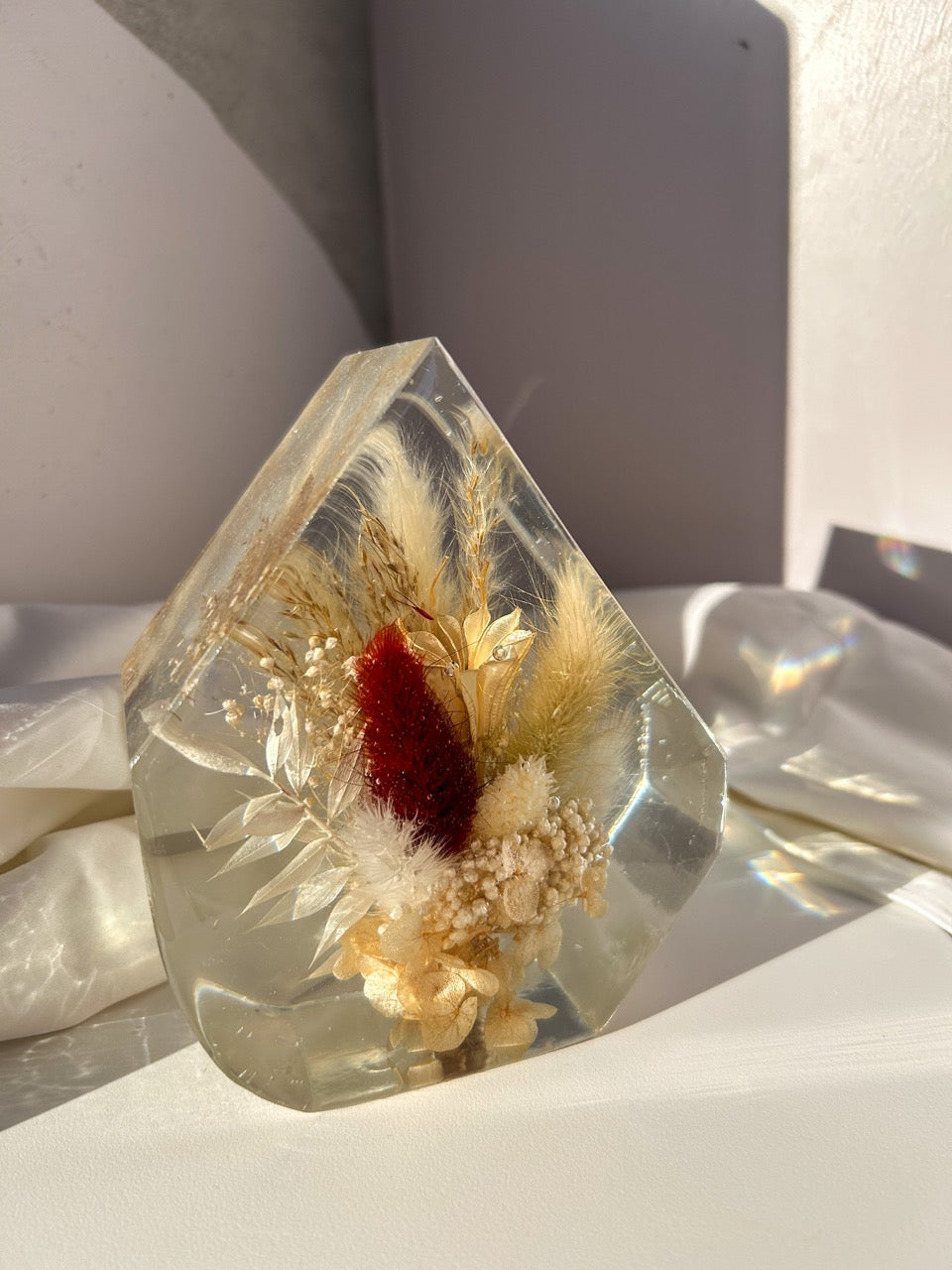 Gem-shaped resin decor featuring a preserved bouquet of dried flowers, including a striking burgundy red flower, all encased in clear resin. Handmade botanical art, perfect for unique home decor or as a thoughtful gift.