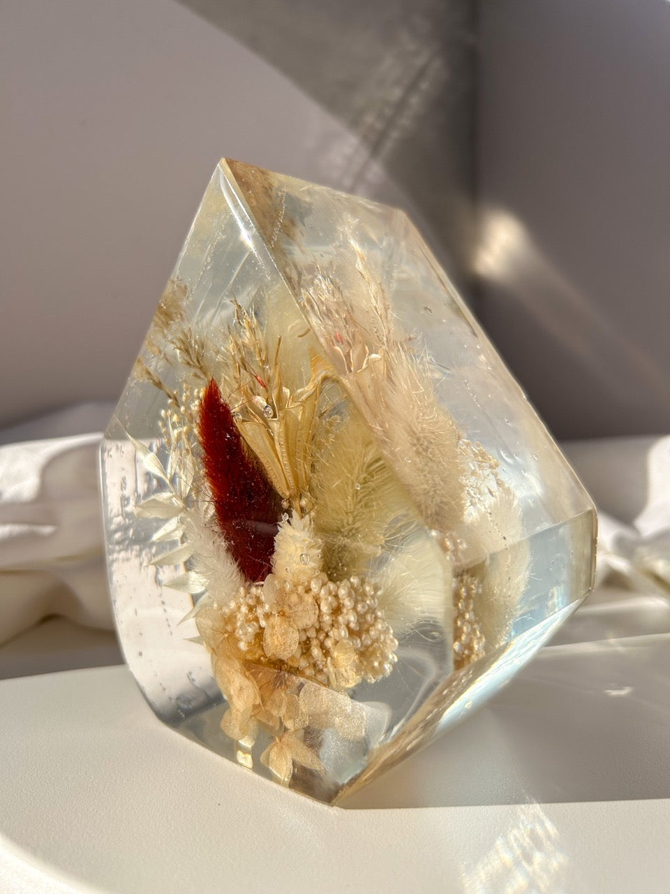 Gem-shaped resin decor featuring a preserved bouquet of dried flowers, including a striking burgundy red flower, all encased in clear resin. Handmade botanical art, perfect for unique home decor or as a thoughtful gift.