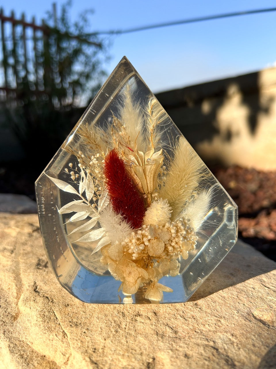 Gem-shaped resin decor featuring a preserved bouquet of dried flowers, including a striking burgundy red flower, all encased in clear resin. Handmade botanical art, perfect for unique home decor or as a thoughtful gift.