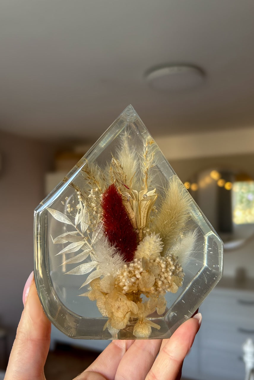 Gem-shaped resin decor featuring a preserved bouquet of dried flowers, including a striking burgundy red flower, all encased in clear resin. Handmade botanical art, perfect for unique home decor or as a thoughtful gift.