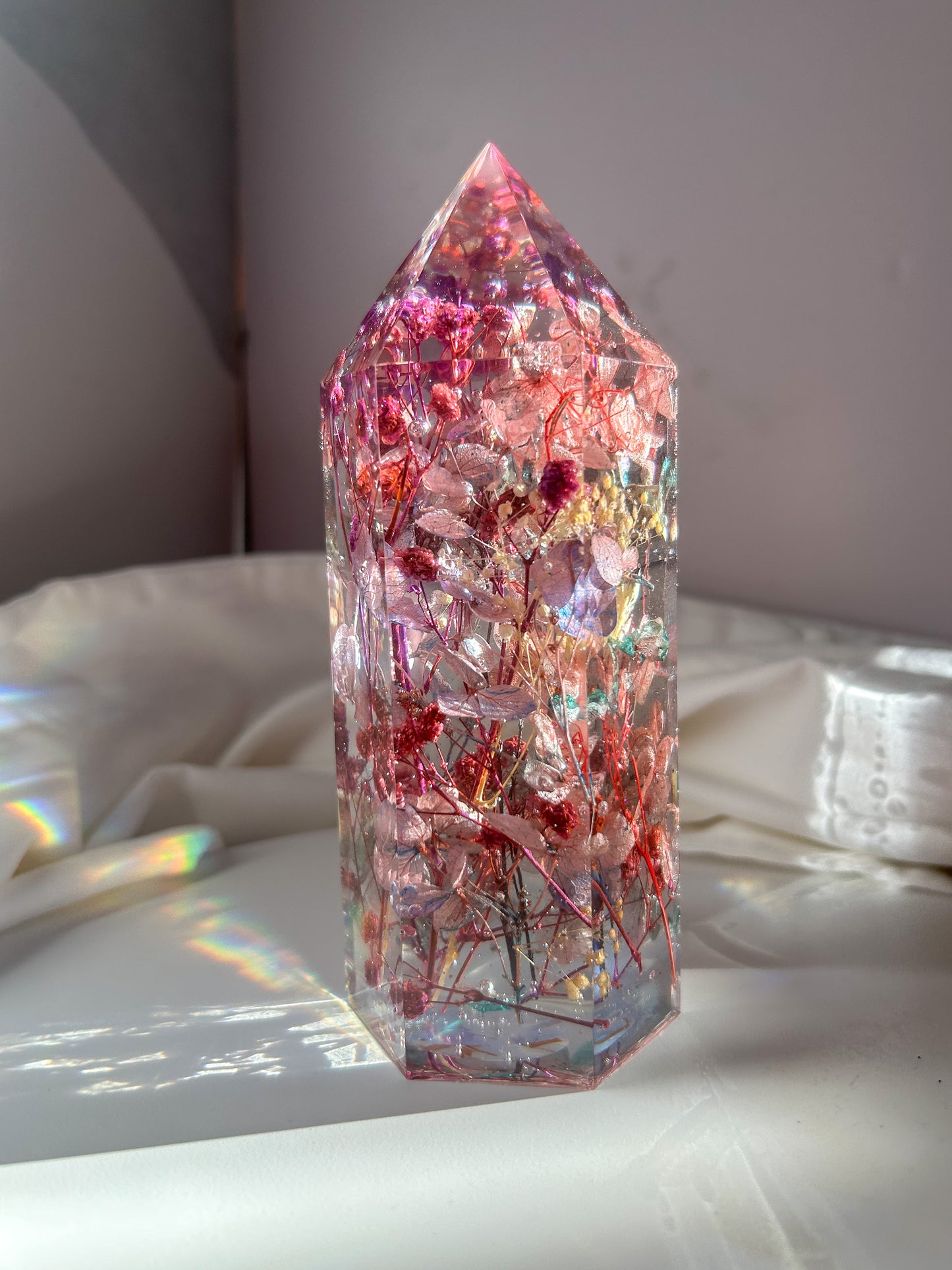 A beautiful crystal resin tower point with real dried flowers the colors of purple pink and a touch of blue beautifully decorates a bedside table and any room. great for gifting as a unique and handmade keepsake present.