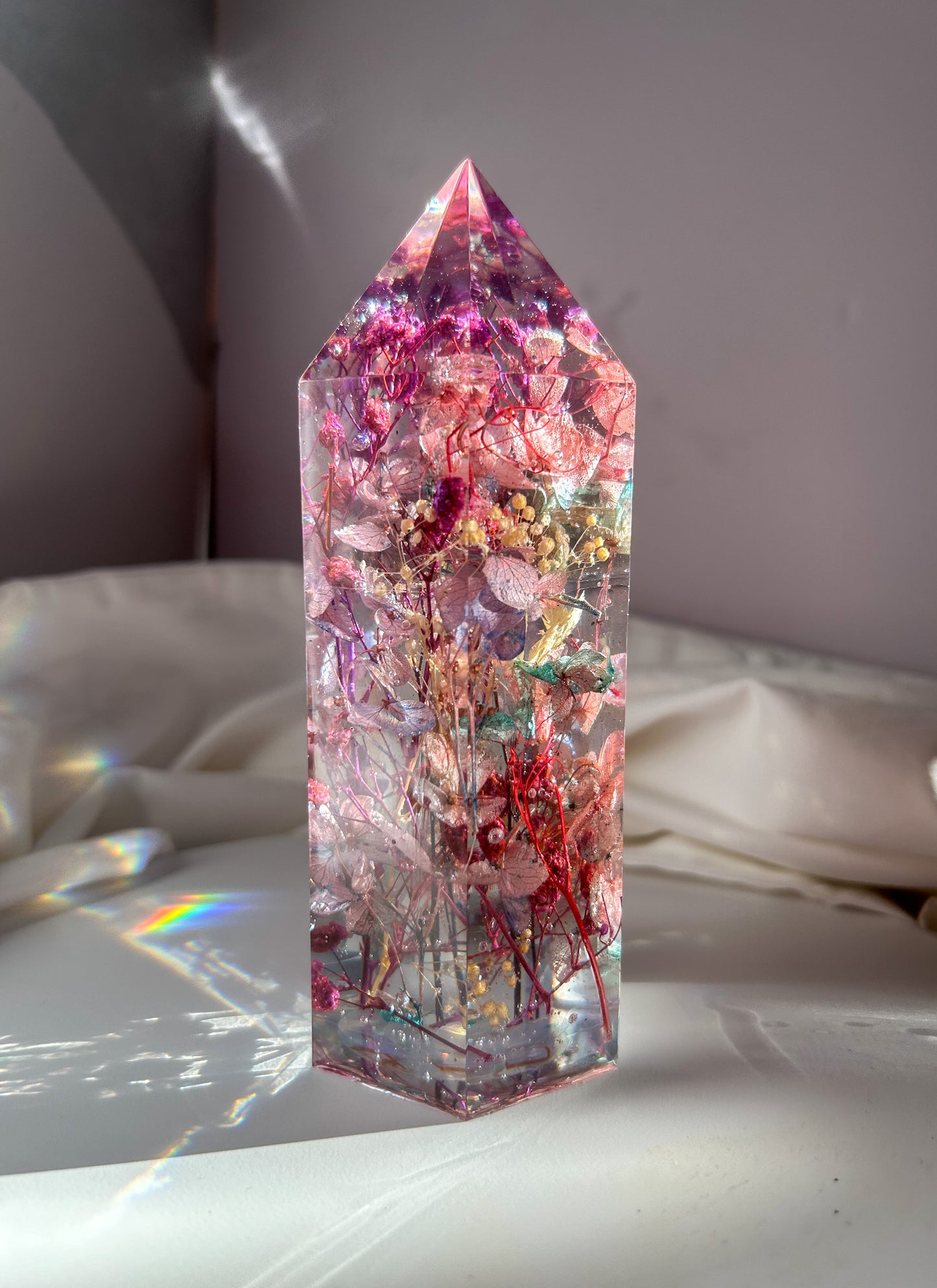 A beautiful crystal resin tower point with real dried flowers the colors of purple pink and a touch of blue beautifully decorates a bedside table and any room. great for gifting as a unique and handmade keepsake present.