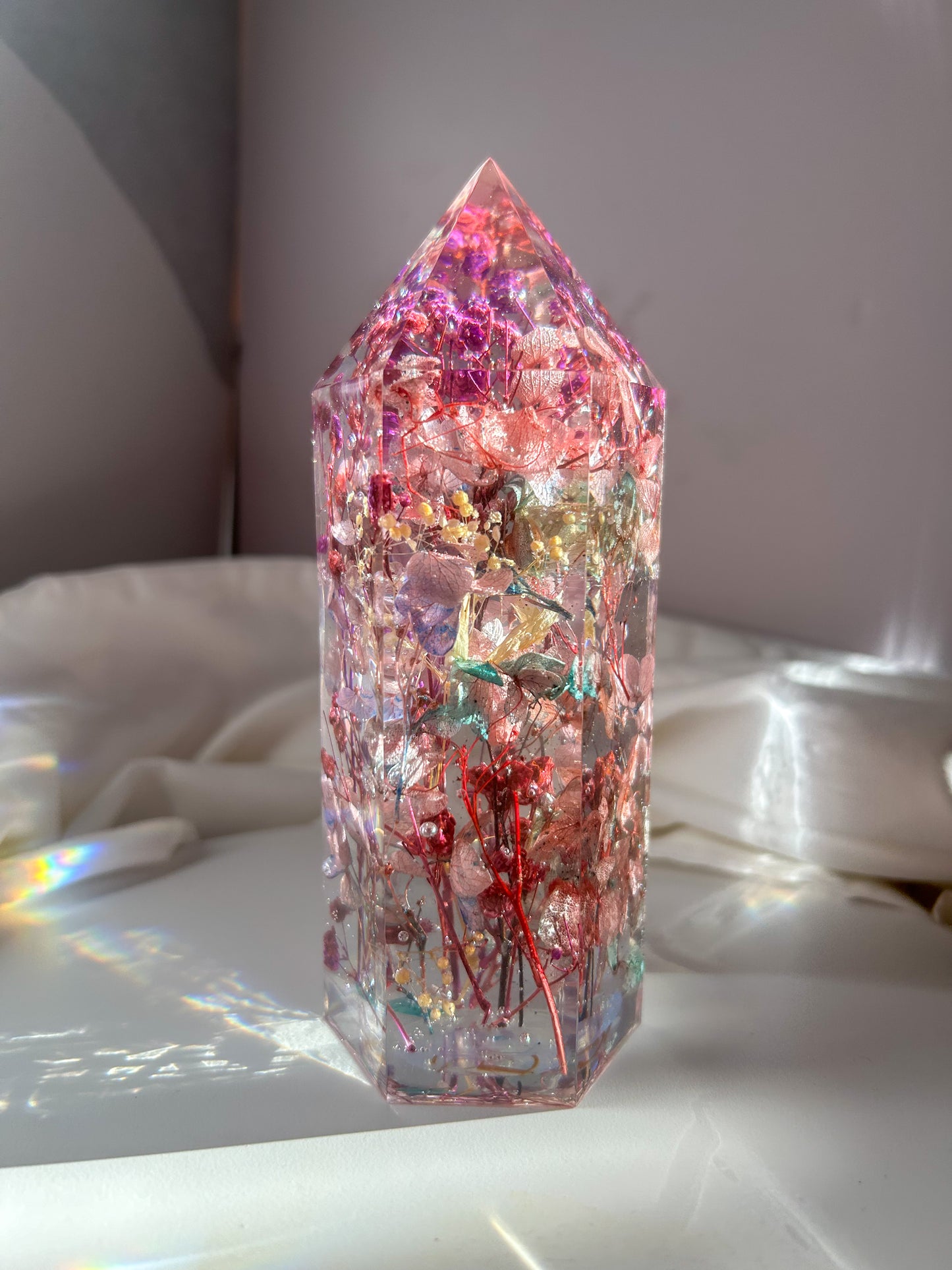 A beautiful crystal resin tower point with real dried flowers the colors of purple pink and a touch of blue beautifully decorates a bedside table and any room. great for gifting as a unique and handmade keepsake present.