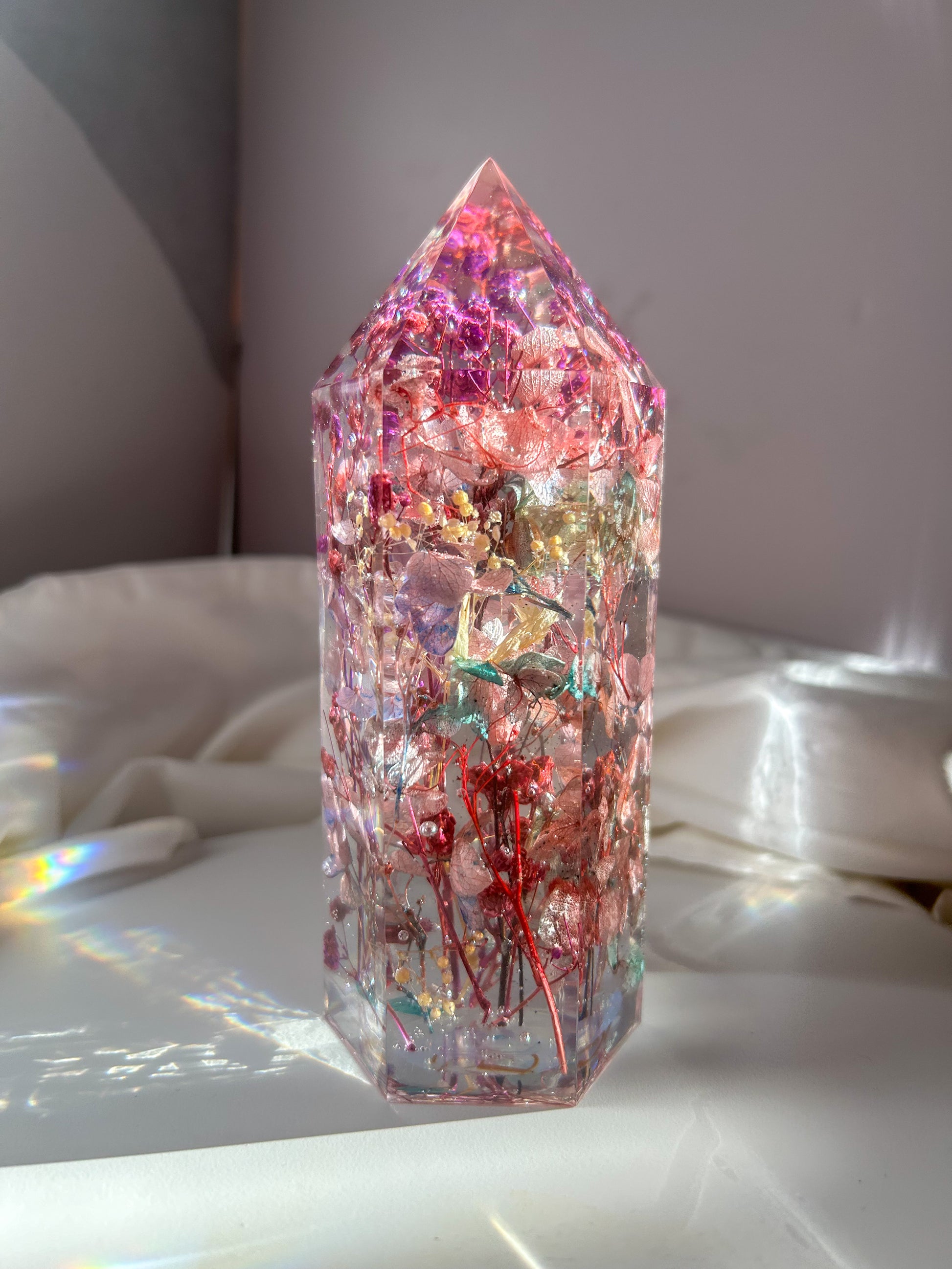 A beautiful crystal resin tower point with real dried flowers the colors of purple pink and a touch of blue beautifully decorates a bedside table and any room. great for gifting as a unique and handmade keepsake present.