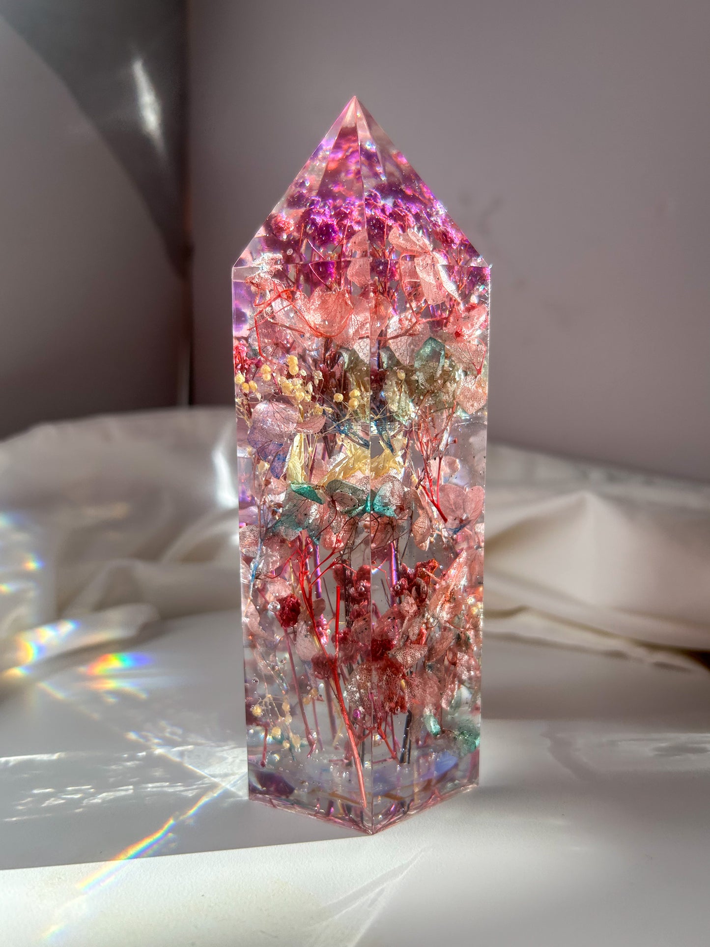 A beautiful crystal resin tower point with real dried flowers the colors of purple pink and a touch of blue beautifully decorates a bedside table and any room. great for gifting as a unique and handmade keepsake present.