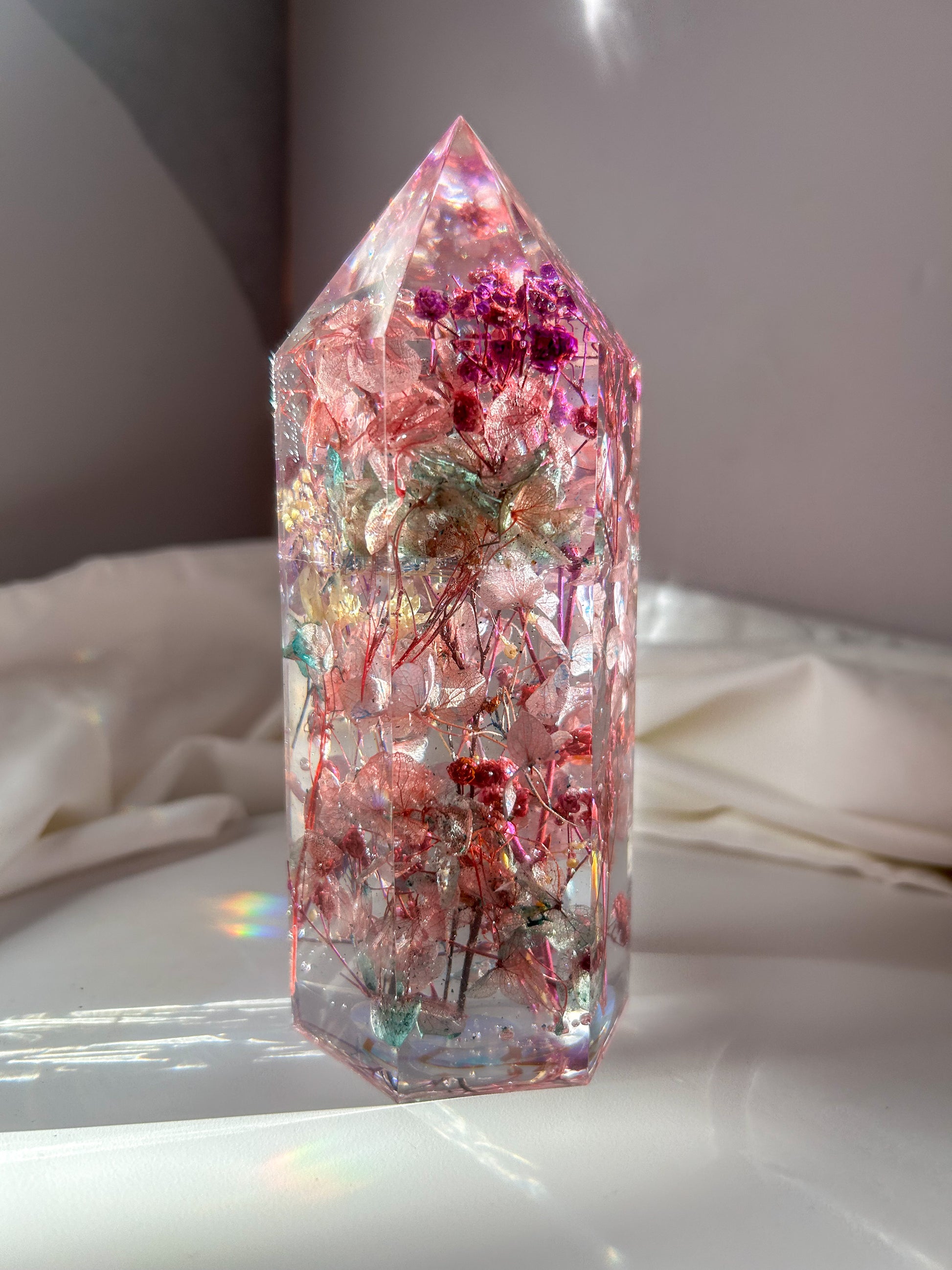 A beautiful crystal resin tower point with real dried flowers the colors of purple pink and a touch of blue beautifully decorates a bedside table and any room. great for gifting as a unique and handmade keepsake present.