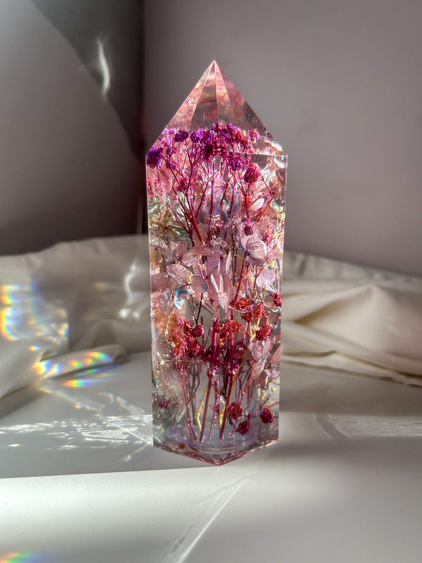 A beautiful crystal resin tower point with real dried flowers the colors of purple pink and a touch of blue beautifully decorates a bedside table and any room. great for gifting as a unique and handmade keepsake present.