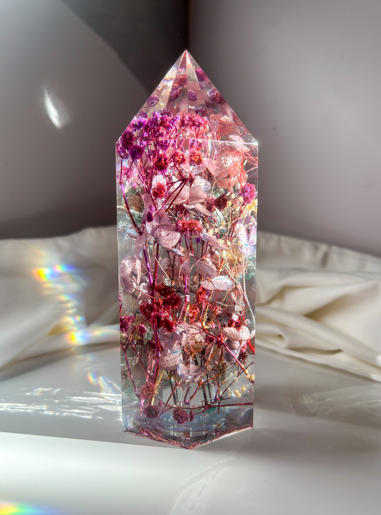 A beautiful crystal resin tower point with real dried flowers the colors of purple pink and a touch of blue beautifully decorates a bedside table and any room. great for gifting as a unique and handmade keepsake present.