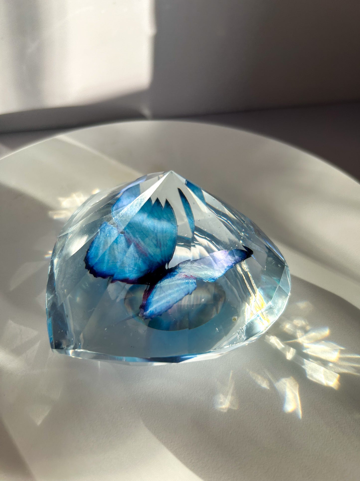 Heart-shaped resin paper holder featuring a faux blue monarch butterfly encased in clear resin. A nature-inspired handmade desk accessory perfect for home office decor or as a unique gift.