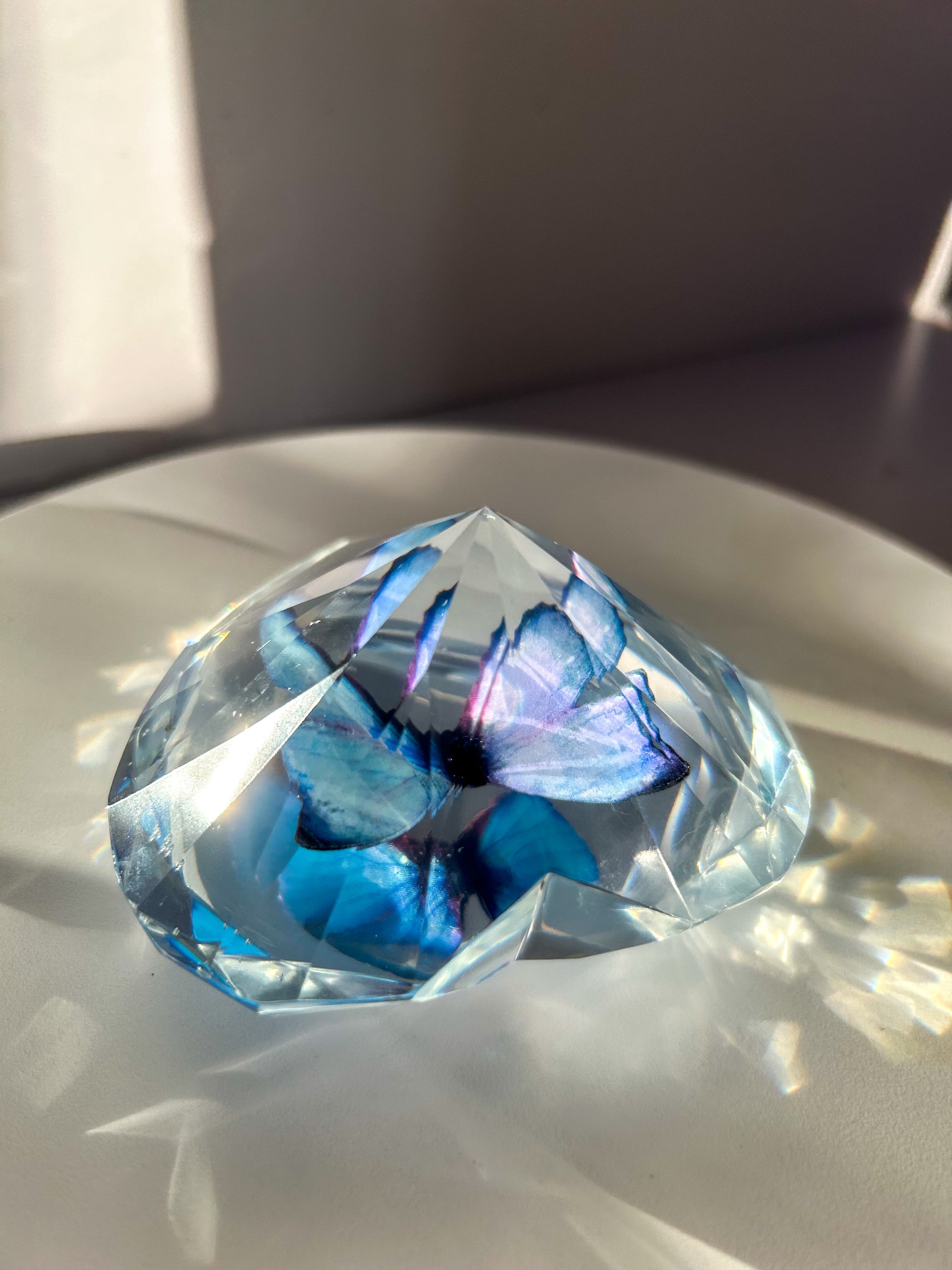 Heart-shaped resin paper holder featuring a faux blue monarch butterfly encased in clear resin. A nature-inspired handmade desk accessory perfect for home office decor or as a unique gift.