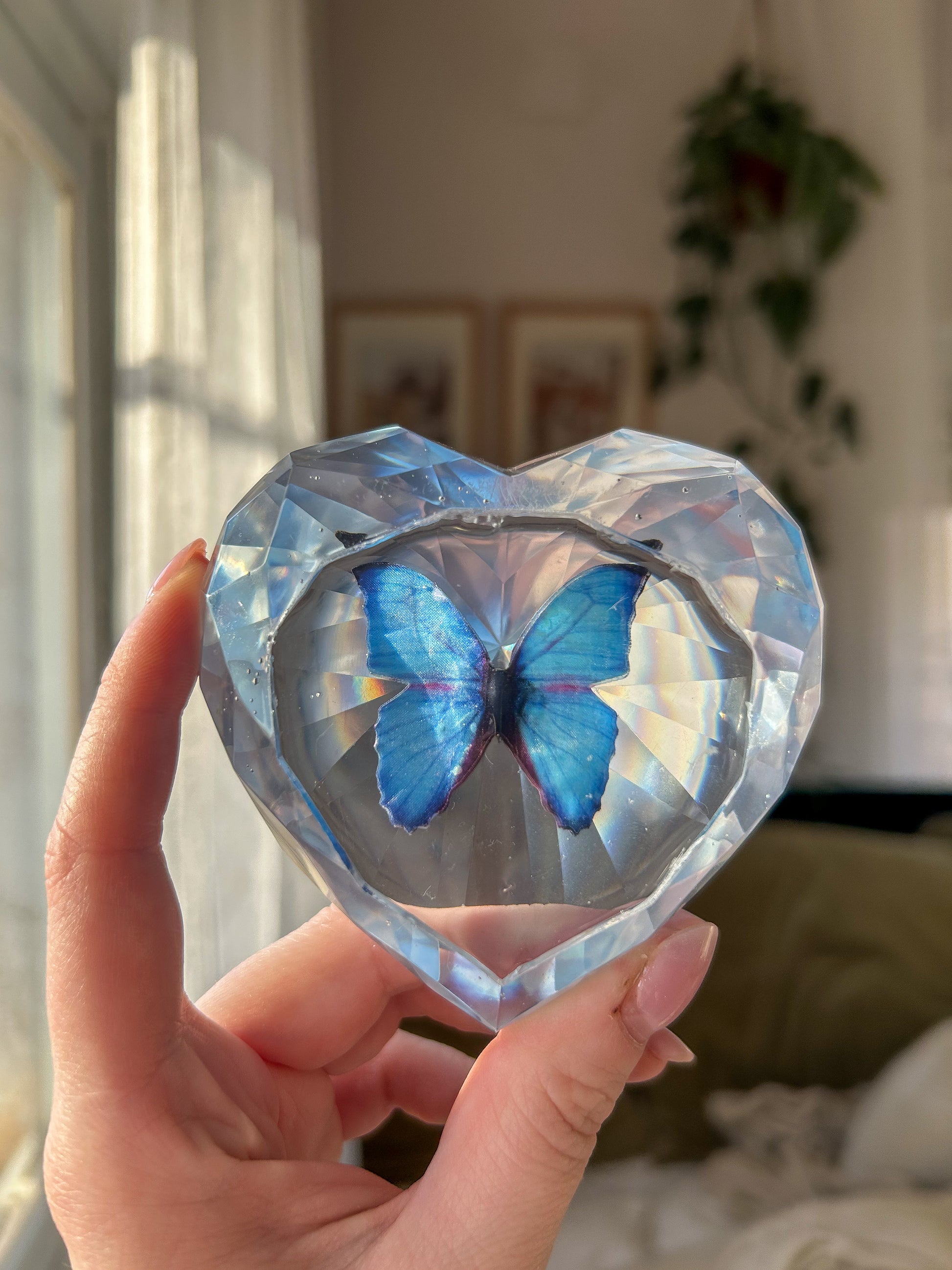 Heart-shaped resin paper holder featuring a faux blue monarch butterfly encased in clear resin. A nature-inspired handmade desk accessory perfect for home office decor or as a unique gift.